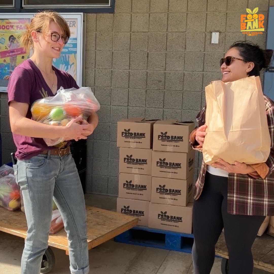 A smiling female Foodbank of Santa Barbara County volunteer giving a woman a bag of vegetables.